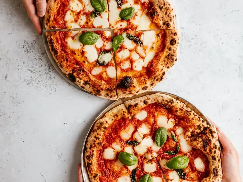 Deux pizzas sortant du four, tenues à la main